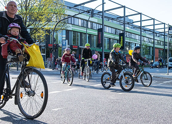 BiciBus in Hamburg Eine Gruppe von Kindern fährt auf ihrer Rädern auf der Straße. Sie werden von Erwachsenen begleitet.